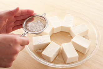 豆腐を耐熱の皿に放射線状に並べる（こうすると、加熱むらが少なくなる）。茶こしで片栗粉をふるい、表面に薄くまぶす。