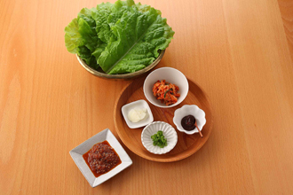 サンチュと薬味を用意する。白菜キムチは食べやすく切り、にんにくは薄切り、青唐辛子は小口切りにし、それぞれ小皿にのせ、コチュジャンも添える。ホットプレートを温めて牛肉を焼いてたれをからめる。サンチュにのせてナムルや塩もみ大根、好みの薬味をのせ、巻いて食べる。