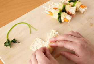 油揚げの野菜巻きを作る。三つ葉は熱湯でさっとゆでる。油揚げは熱湯をかけて水気を切り、長さを4等分に切って開く。中面を上にしておき、にんじん、えのきだけを等分にのせてくるくると巻き、三つ葉でしばる。