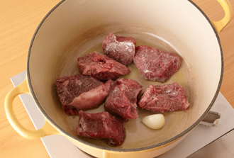 玉ねぎは薄切りにする。マッシュルームは石づきを取る。にんにくはつぶす。牛肉に塩、こしょうを各少々ふり、小麦粉を薄くまぶす。鍋にオリーブ油とにんにくを入れて中火で炒め、香りが出たら牛肉を加えて表面を焼きつける。