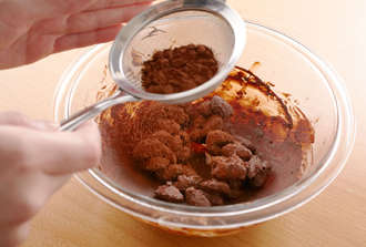 別のボウルに冷ましたアーモンドを入れ、溶かしたチョコレートの1/5量を加えてからめる。ボウルの中で広げて少しさまし、チョコレートが固まったら再び少量ずつ入れる。これを4回繰り返し、チョコレートの層を重ねる。最後にココアパウダーを茶こしでふるい入れて全体にまぶす。