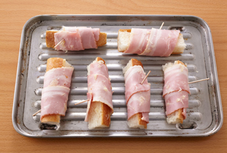 ベーコンに薄くにんにくを塗ってオーブントースターの天板にのせ、ベーコンが焼けるまでときどき上下を返しながら5～6分焼く。楊枝を外し、熱いうちにドライバジルをふって器に盛る。