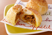 ナン生地でキーマカレーを包んで焼けば、焼きカレーパンのでき上がり！表面にパン粉をつけるとこんがりサクサクになります。作り方：ナンの生地1/6量を丸く広げ、キーマカレー1/6量をのせて包む（包み終わりはしっかり閉じて）。形をととのえ、溶き卵を薄く塗ってパン粉をふり、オーブン用シートを敷いた天板にのせる。かたく絞った濡れ布巾をかけ、10分休ませる。サラダ油適量を回しかけ、200度のオーブンで13～14分焼く。