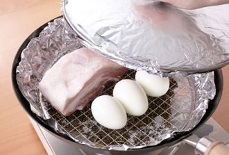 焼き網の上に豚肉、ゆで卵をのせる。燻煙で色や香りがつくためアルミホイルを巻きつけたふたをして、強火に2～3分かける。煙が出てきたら弱めの中火にし、さらに25～30分燻煙する。豚肉に火が通ったら火を止める。竹串を刺してみて、透明な肉汁が出ればOK。粗熱がとれたら食べやすく切る。皿に盛り、星型で抜いたパプリカを散らし、クレソンを添える。