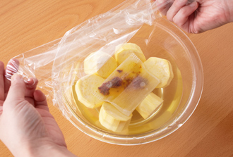 さつまいもは皮を厚めにむいて厚さ2センチの輪切りにし、水に30分ほどさらしてアクを抜き、水気をきる。くちなしの実をお茶パックに入れ、めん棒などでたたいて実を砕く。さつまいもを耐熱のボウルに入れてくちなしのパックをのせ、かぶるくらいの水を注いで、ラップをかけて電子レンジ600Wで15分加熱する。