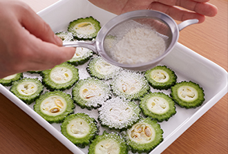 ゴーヤをバットに並べて両面に塩をふる。茶こしを使って薄力粉をふり、両面に薄くまぶす。