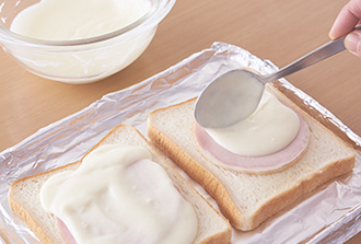 食パンの片面にバターを塗っておく。オーブントースターの天板に、バターを塗った面を上にして食パン2枚を並べ、ハムを2枚ずつ重ねる。その上にチーズソースを1/4量ずつのせる。残りの食パンをサンドするように1枚ずつのせ（バターを塗った面を下）、さらにチーズソースを等分に塗って粗挽き黒こしょうをふる。ピザチーズを等分にのせ、オーブントースター（1000W）で焼き色がつくまで焼く。半分に切って器に盛る。